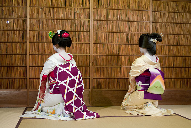 Un hombre con un kimono japonés en la cabeza se para frente a una pared que  dice 'geisha'.